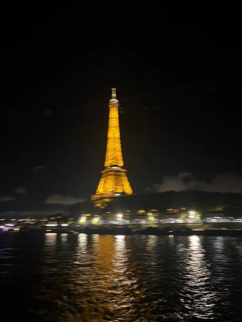 A blurred photo of the golden lit Eiffel Tower and its reflection, taken from the river at night