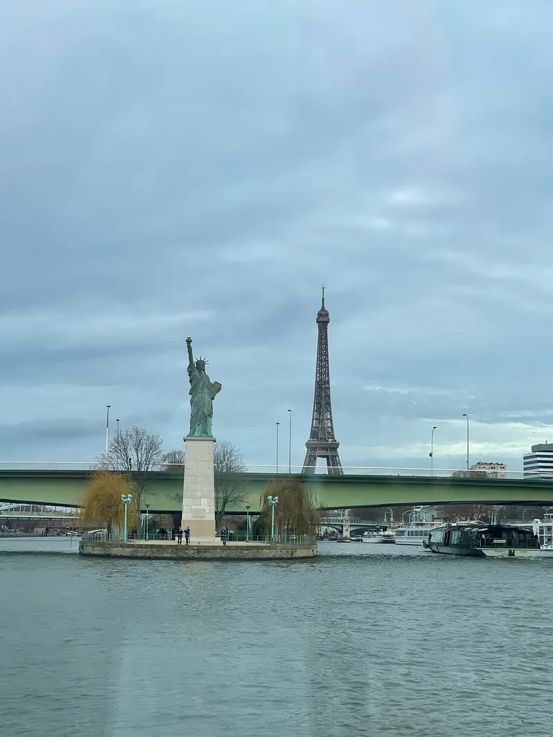The Statue of Liberty replica on its island in the Seine, with the Eiffel Tower behind under a grey sky