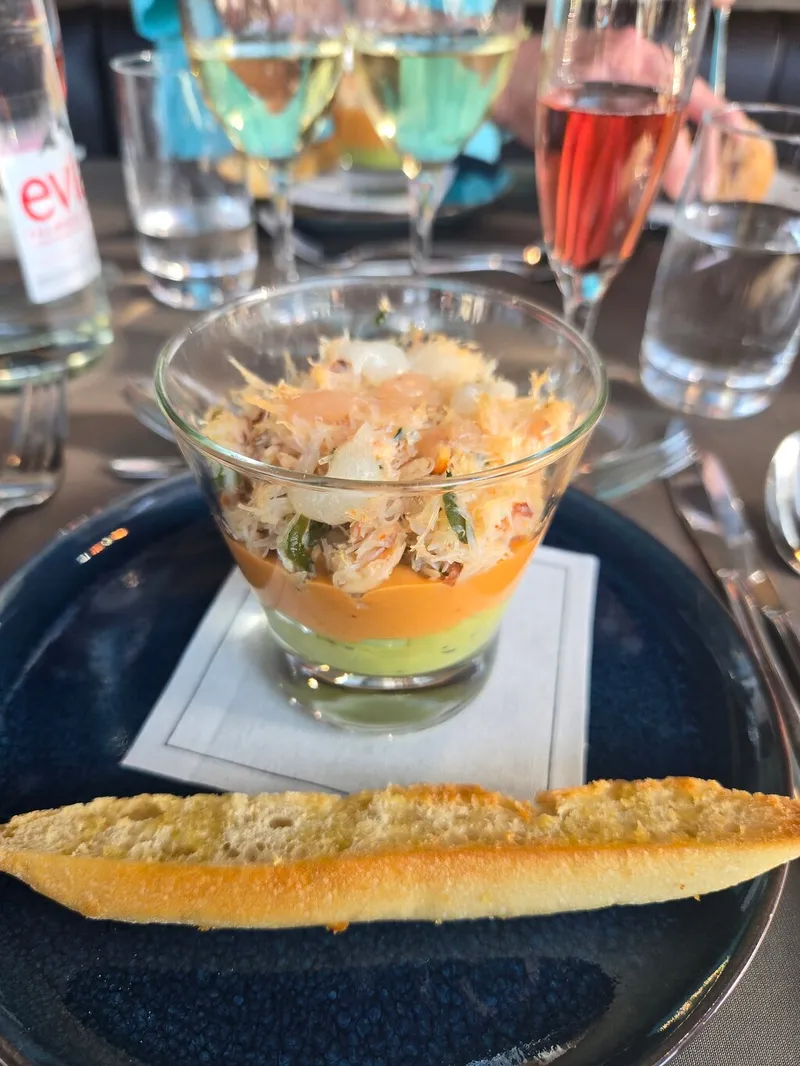 A layered crab starter in a glass with toasted bread, with glasses of white wine and kir behind it