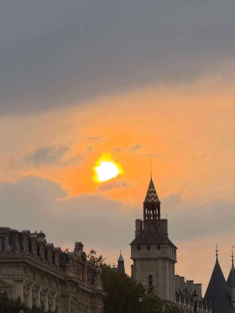 The sun setting behind Paris rooftops and a dome seen from the Seine