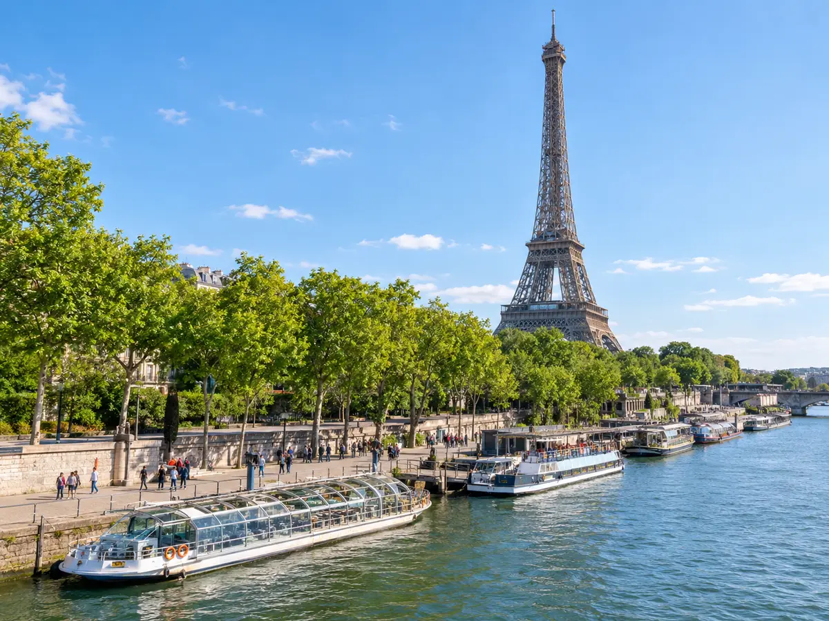 Glass-roofed sightseeing boats moored along a tree-lined quay below the Eiffel Tower